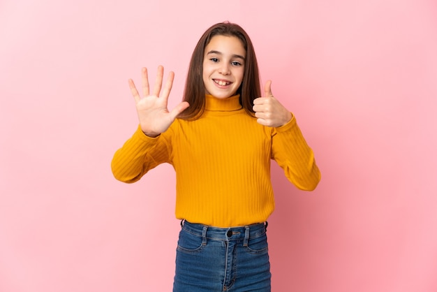 Niña aislada en la pared rosa contando seis con los dedos