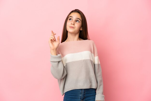 Niña aislada en la pared rosa con los dedos cruzando y deseando lo mejor