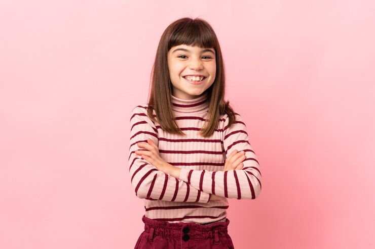 Foto niña aislada en pared rosa manteniendo los brazos cruzados en posición frontal