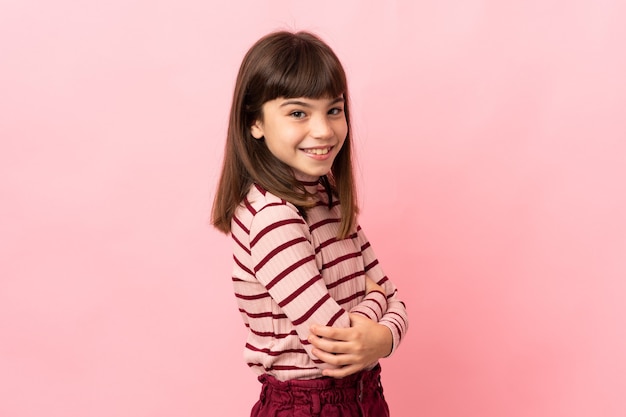 Niña aislada en la pared rosa mirando hacia el lado y sonriendo