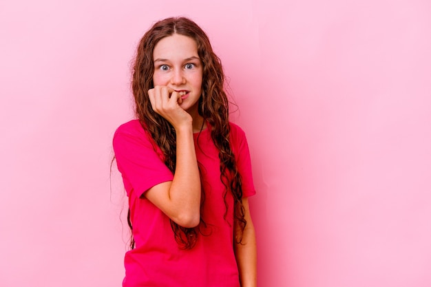 Niña aislada en la pared rosa mordiéndose las uñas, nerviosa y muy ansiosa