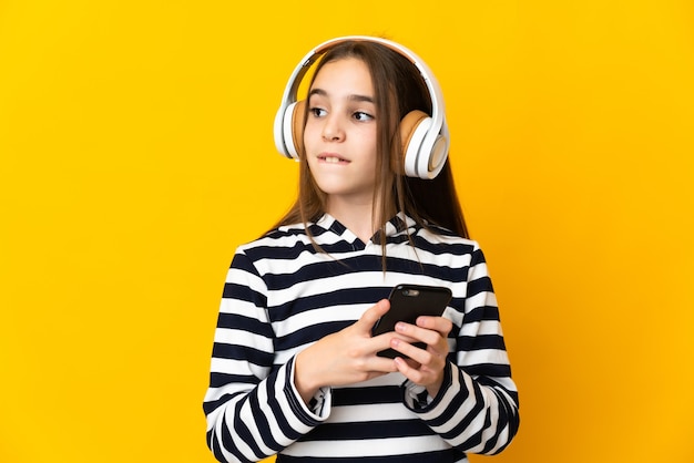 Niña aislada sobre fondo amarillo escuchando música con un móvil y pensando