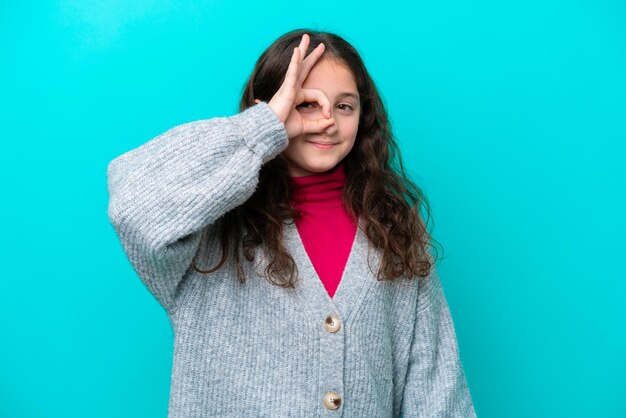 Niña aislada sobre fondo azul que muestra el signo ok con los dedos