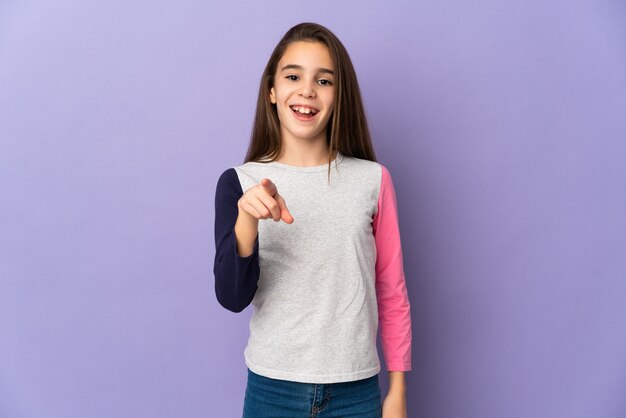 Niña aislada sobre fondo púrpura sorprendido y apuntando al frente