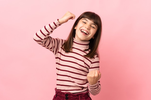 Niña aislada sobre fondo rosa celebrando una victoria