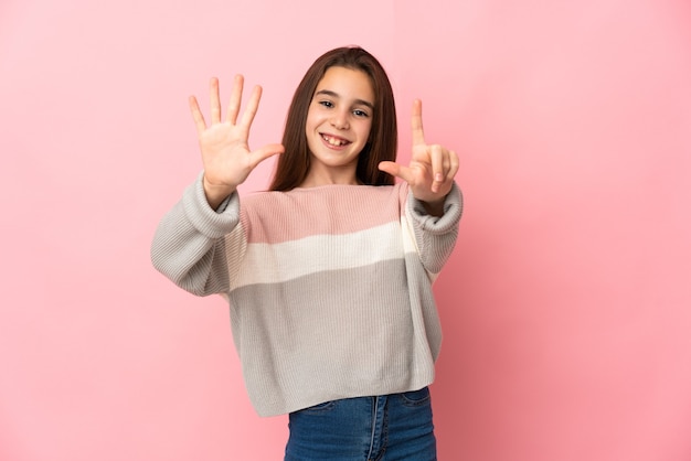 Niña aislada sobre fondo rosa contando siete con los dedos