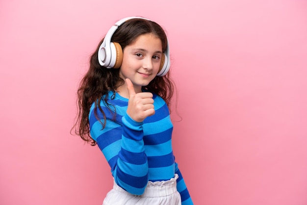 Niña aislada sobre fondo rosa escuchando música y con el pulgar hacia arriba