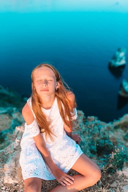 Niña al aire libre en el borde del acantilado disfruta de la vista en la cima de la montaña al atardecer