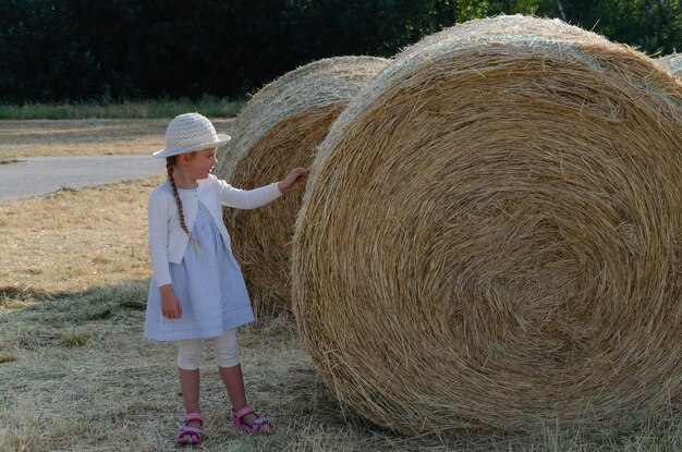 Una niña al lado de un gran balde de heno