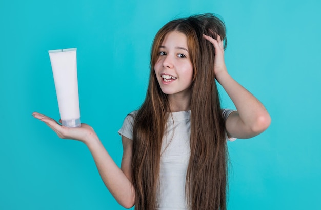 Niña alegre con cabello largo y liso, champú acondicionador o botella de gel, cuidado del cabello.