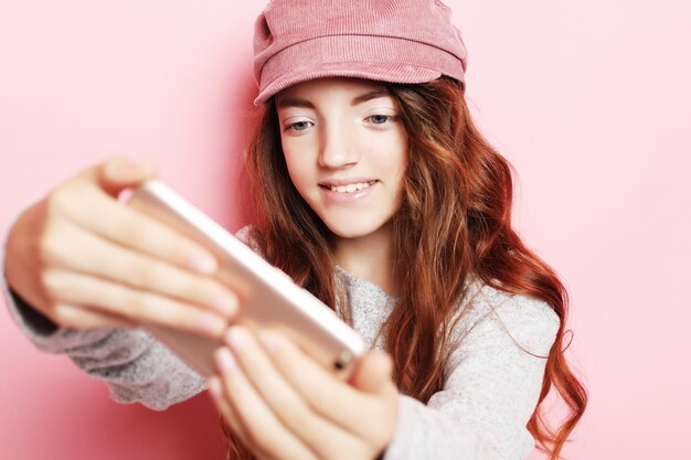 Niña alegre con cabello rizado l tomando un selfie aislado sobre fondo rosa