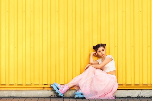 Una niña alegre come helado y rueda sobre rodillos en verano contra la de una pared amarilla