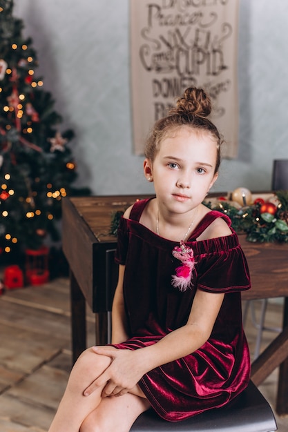 Niña alegre en decoración navideña con té en casa acogedora con coloridas luces de año nuevo