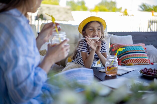 Niña alegre disfrutando del desayuno con la madre en la terraza al aire libre, pasar tiempo juntos