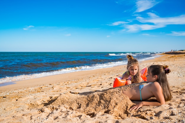 Niña alegre enterrar a su hermana mayor en la arena mientras juega en la playa