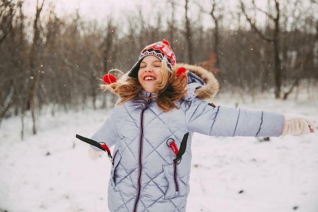 Niña alegre feliz divirtiéndose en el bosque en un día de invierno. niño juega con nieve.