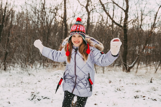 Niña alegre feliz divirtiéndose en el bosque en un día de invierno. niño juega con nieve.