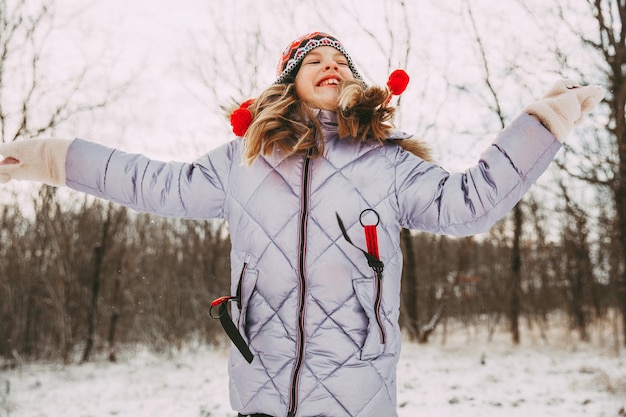 Foto niña alegre feliz divirtiéndose en el bosque en un día de invierno. niño juega con nieve.