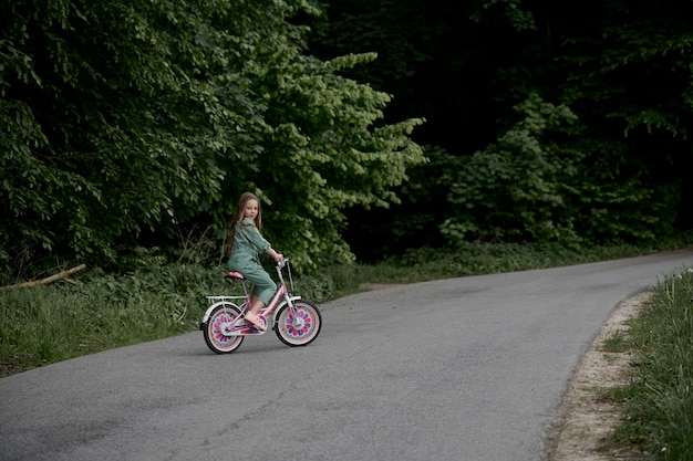 Niña alegre feliz montando en bicicleta en el parque en la naturalezaxD