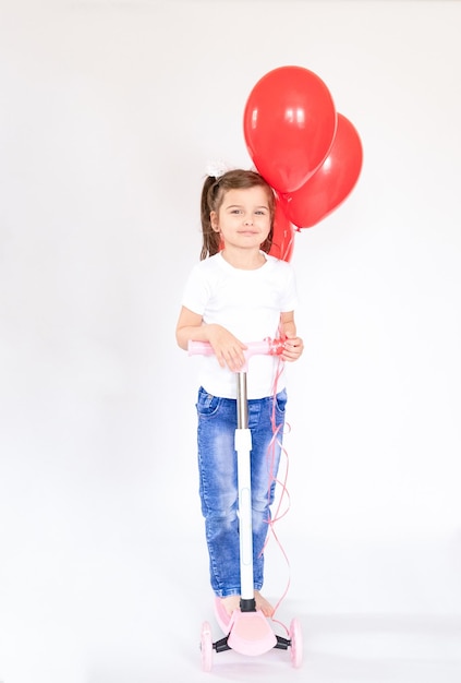 Niña alegre con globos rojos Chica montando un scooter Aislado sobre fondo blanco