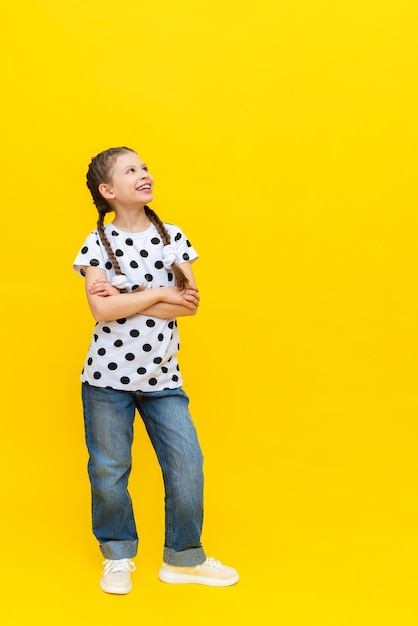 Una niña alegre con hermosas coletas largas en jeans sobre un fondo amarillo