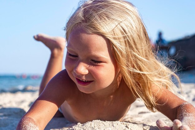 Niña alegre se juega acostado en la playa de arena en un día soleado.