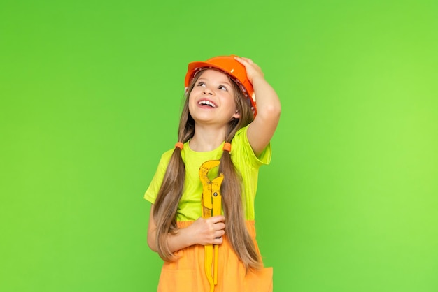 Una niña alegre con una llave ajustable en las manos mira hacia arriba y sostiene un casco protector con la mano. Reparación y construcción. fondo aislado.