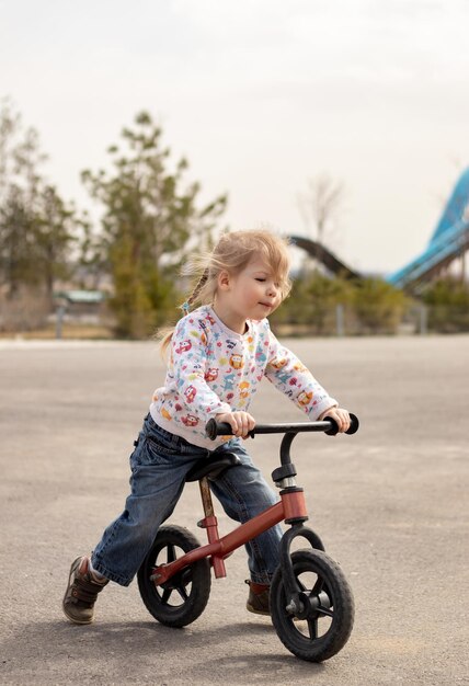 Foto niña alegre montando una bicicleta en el parque de la ciudad en un día soleado al aire libre