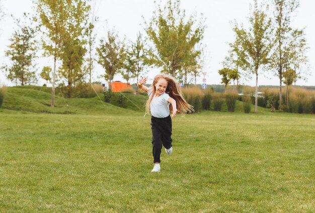 Una niña alegre con el pelo largo corre por la hierba en el parque y se regocija