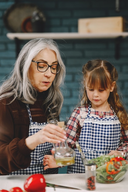 Niña alegre que se divierte con la abuela jubilada al cocinar