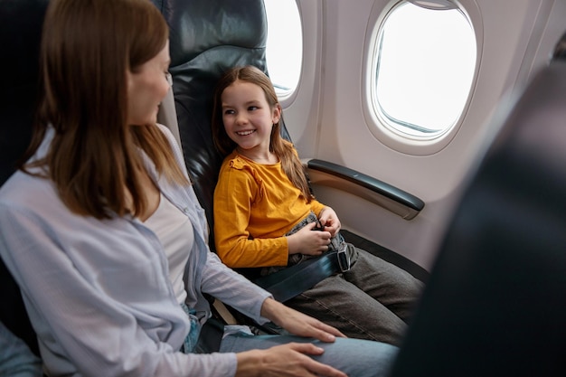 Niña alegre sentada junto a la madre en el avión de pasajeros