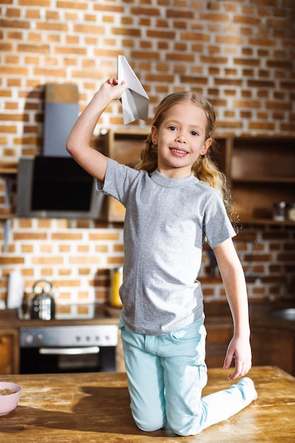 Niña alegre sonriendo y jugando con un avión de papel