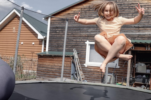 Niña alegre con una sonrisa en la cara con un hermoso vestido saltando en el trampolín