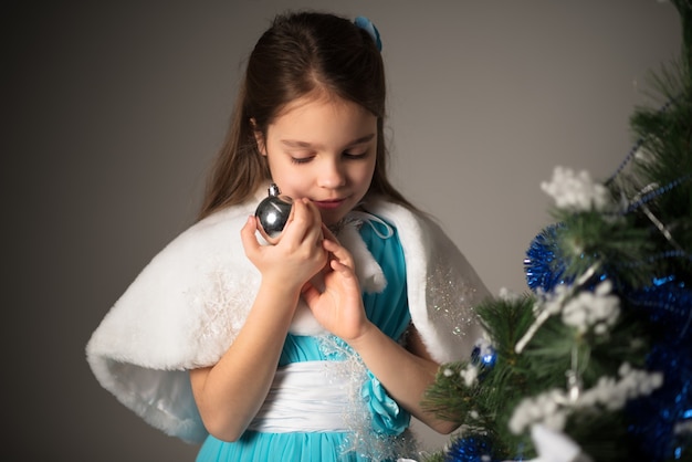 Niña alegre sosteniendo una bola de plata para el árbol de Navidad y pide un deseo