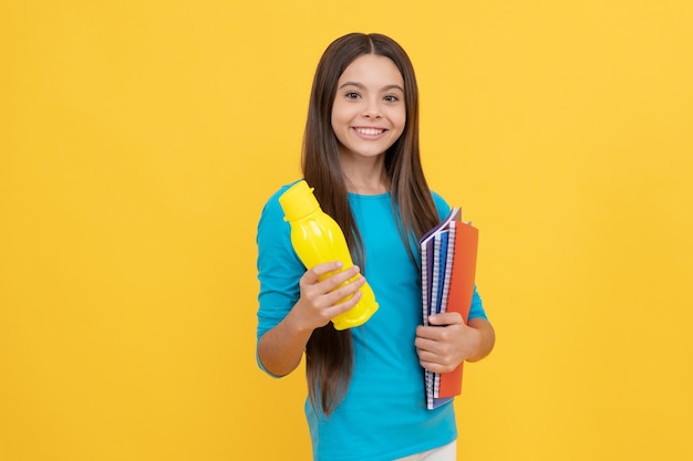 Niña alegre sostiene un bloc de notas para la tarea y el almuerzo con una botella de jugo