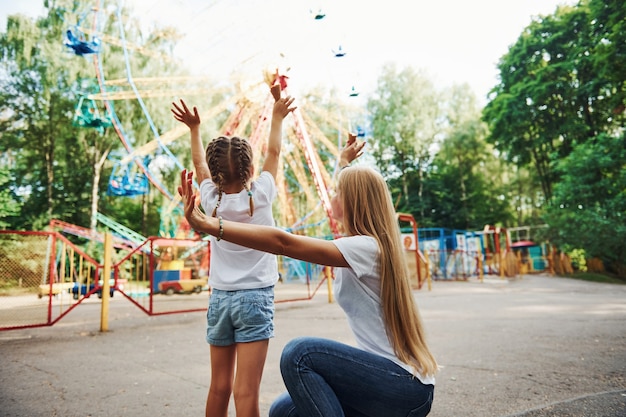 Niña alegre su madre pasar un buen rato en el parque juntos cerca de atracciones