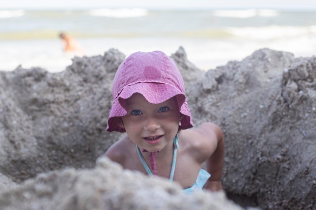 Niña alegre en traje de baño se juega con arena en la playa