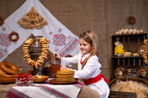 Niña alegre con traje nacional sirviendo té de samovar mientras celebra Maslenitsa