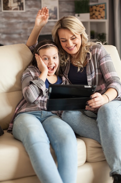 Niña alegre durante una videollamada en tableta con sus abuelos sentados en el sofá con su madre.