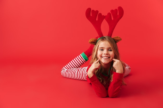 Niña alegre vistiendo traje de ciervo de Navidad sentado aislado