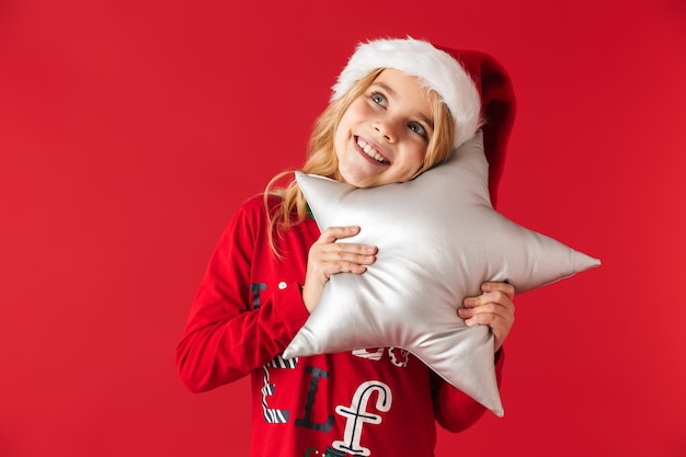 Niña alegre vistiendo traje de Navidad que se encuentran aisladas, sosteniendo una almohada en forma de estrella