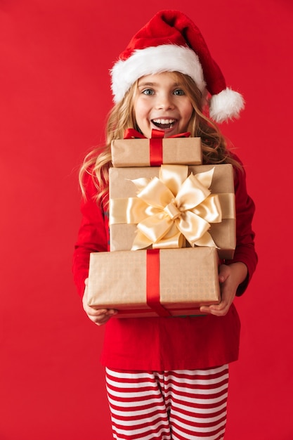 Niña alegre vistiendo traje de Navidad que se encuentran aisladas, sosteniendo cajas de regalo