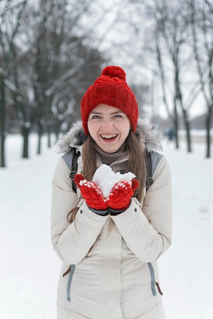 Niña alegre en Winter Park tiene nieve en sus palmas. Retrato de mujer con sombrero rojo tejido.