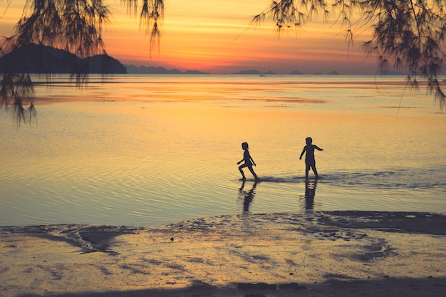 Niña alejándose de su novio en aguas poco profundas al atardecer en la playa