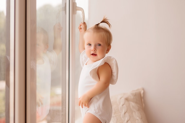 la niña se para en el alféizar de la ventana y mira por la ventana