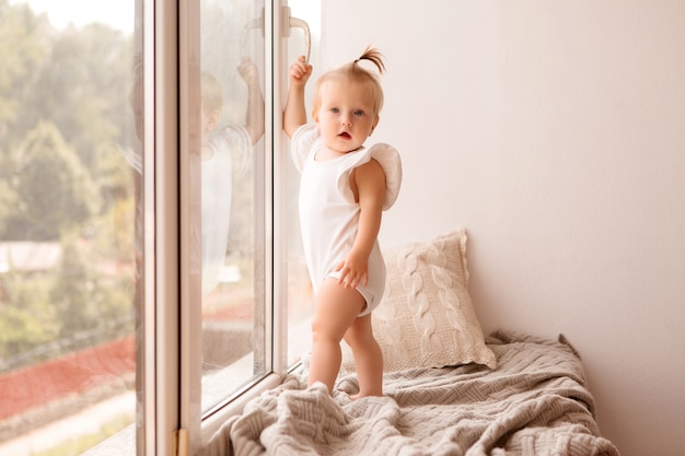 La niña se para en el alféizar de la ventana y mira por la ventana