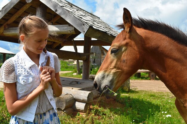 Niña alimenta un caballo con las manos en el pueblo.