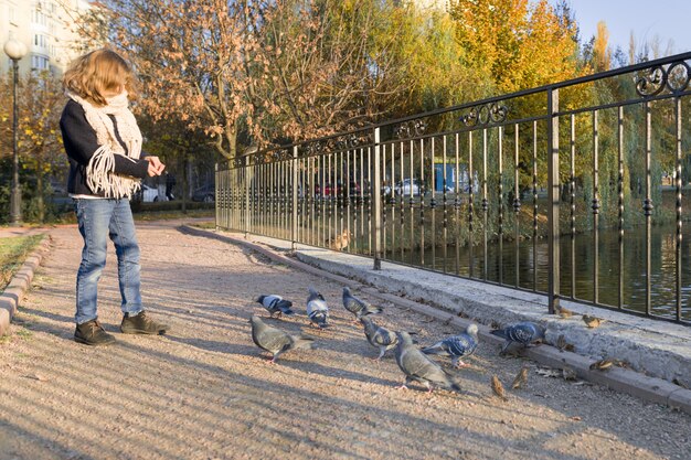 Niña alimentando palomas en el soleado parque de otoño