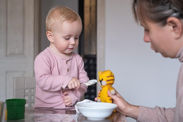 Niña alimentando tigre de juguete con cuchara durante el desayuno