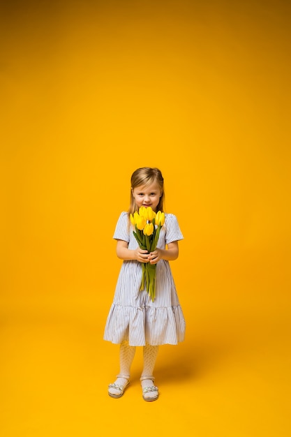 Una niña de altura completa se encuentra con un ramo de tulipanes amarillos sobre amarillo